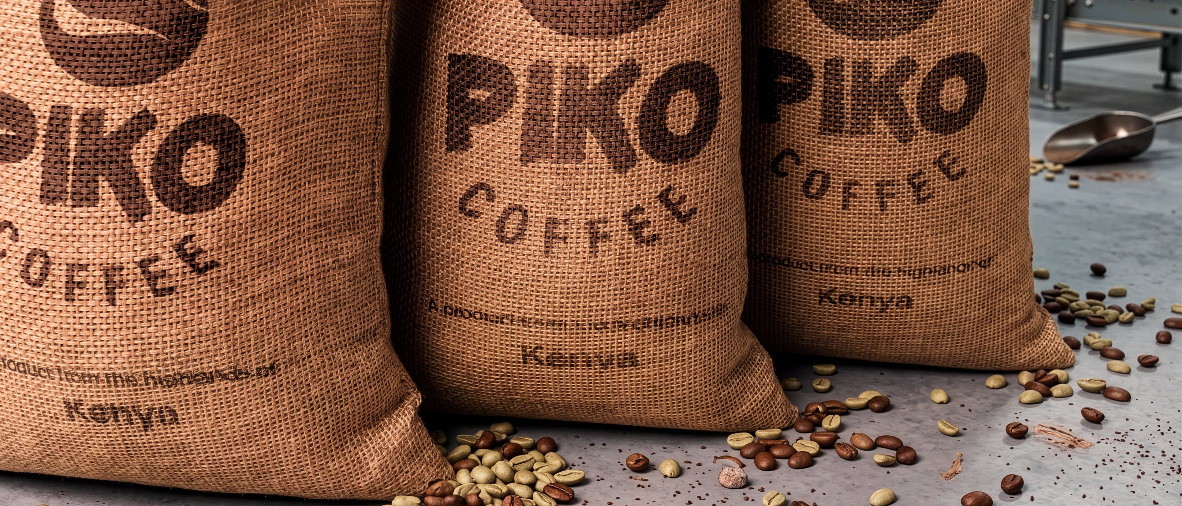Three jute sacks printed with the Piko Coffee mark and the word Kenya, standing side by side with roasted beans scattered across the floor in front of them.